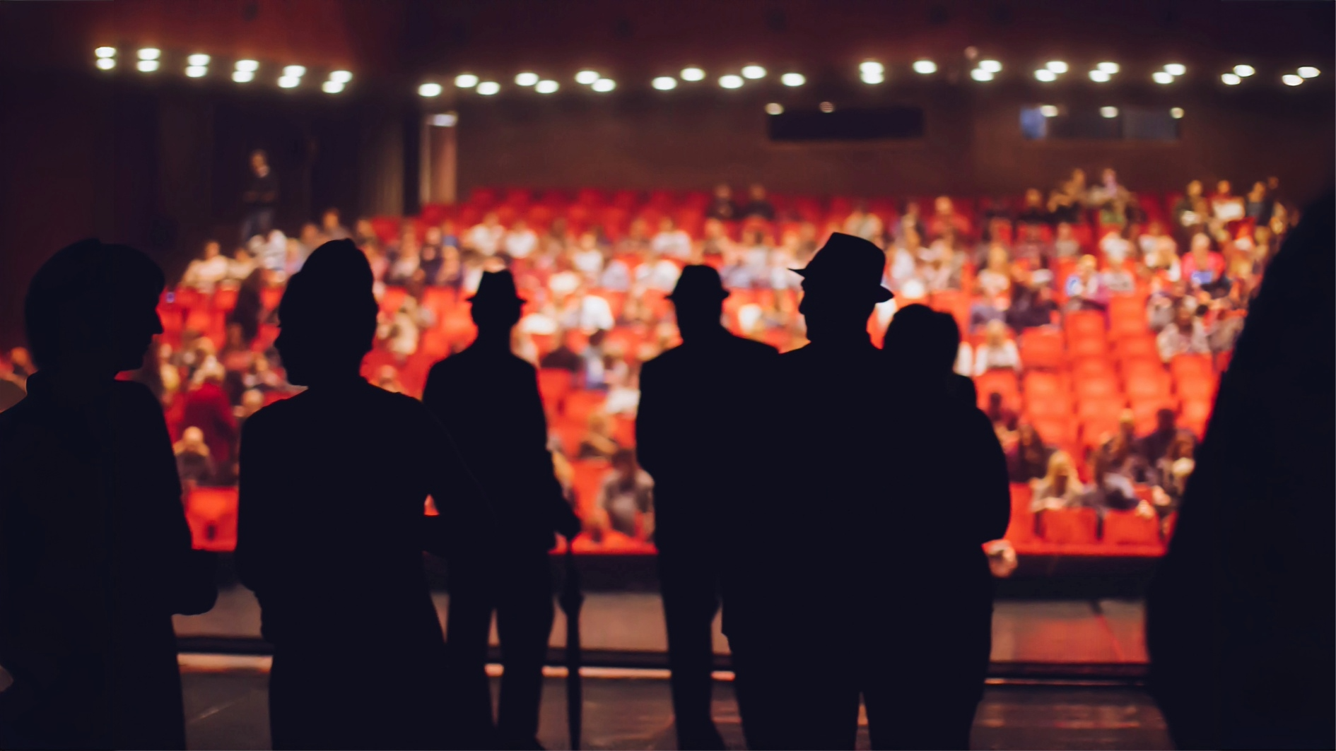 Persone di spalle su un palco di un teatro con sedili della platea nello sfondo